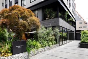 上野諾嘉飯店 (NOHGA HOTEL UENO TOKYO) 充滿自然綠意的入口外觀，以現代洗鍊的深色建築材質搭配豐富植栽，在熱鬧的上野商圈中打造出一座極具質感的靜謐綠洲。